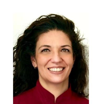 Donna sorridente con capelli ricci e giacca rossa, esprime calore e gentilezza.